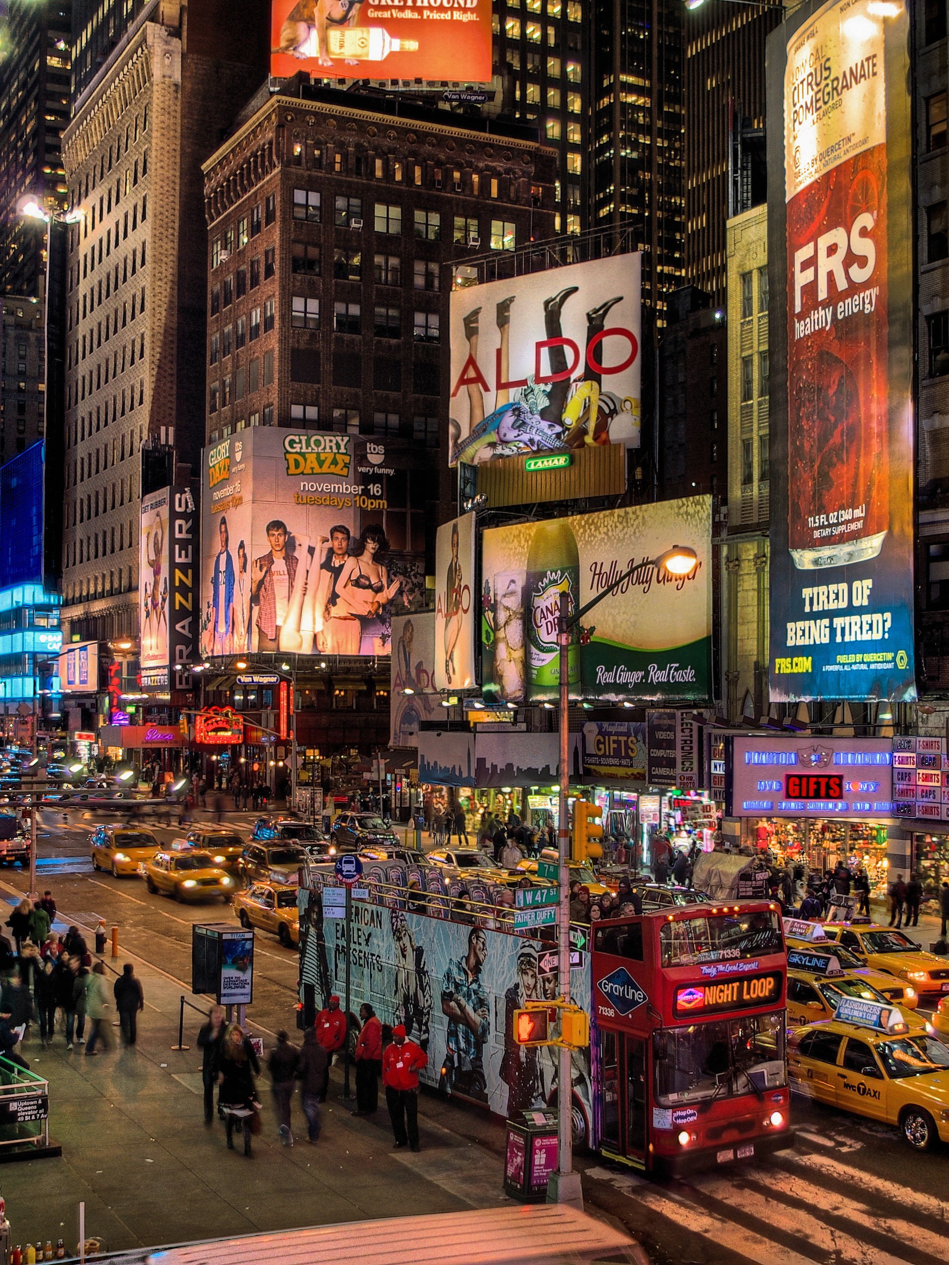 Times Square at night, bustling with bright billboards and neon lights. Crowds and yellow taxis fill the streets, creating a vibrant, energetic atmosphere.
