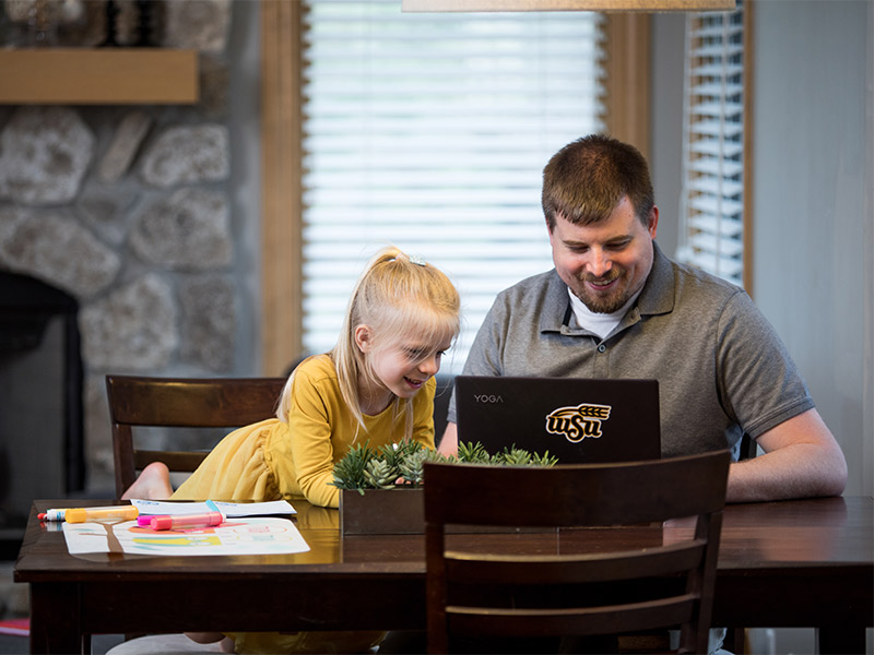 dad taking online class at home with elementary aged daughter beside him