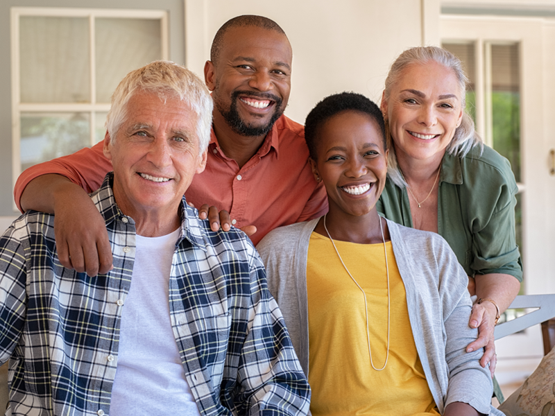 4 retired friends sitting outside on a porch smiling at the camera