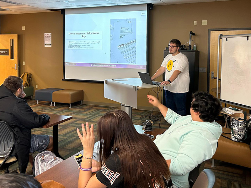A photo of a Shocker Financial Wellness peer counselor lecturing to a group of students.