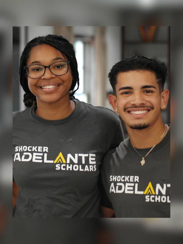 A photo of two smiling Shocker Adelante scholars standing side by side while wearing grey Shocker Adelante T-shirts