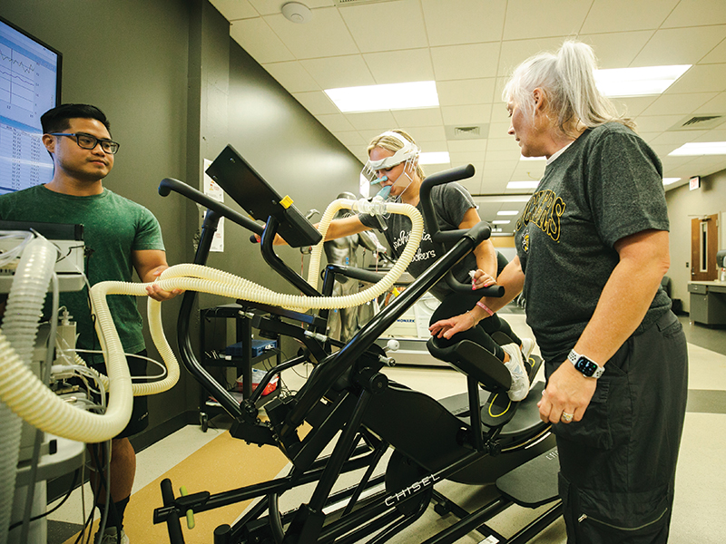 A professor and two students run an exercise test in the Human Performance Studies lab.