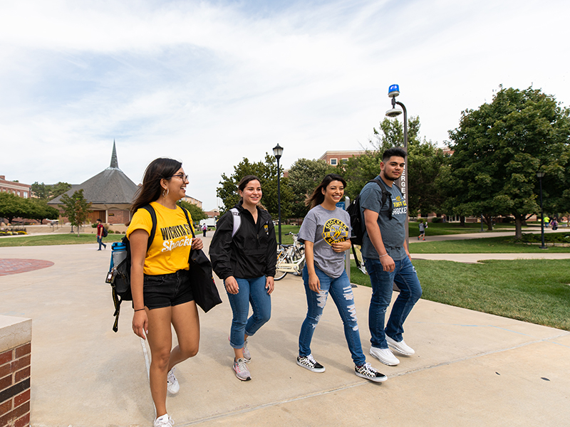 Four students walk outside on campus near the Rhatigan Student Center east patio.