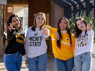 Four students in Shocker gear pose for a photo in the breezeway of McKnight Art Center