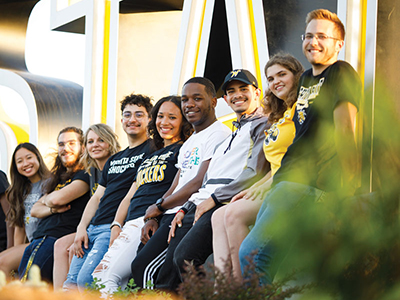 Four students in Shocker gear pose for a photo in the breezeway of McKnight Art Center