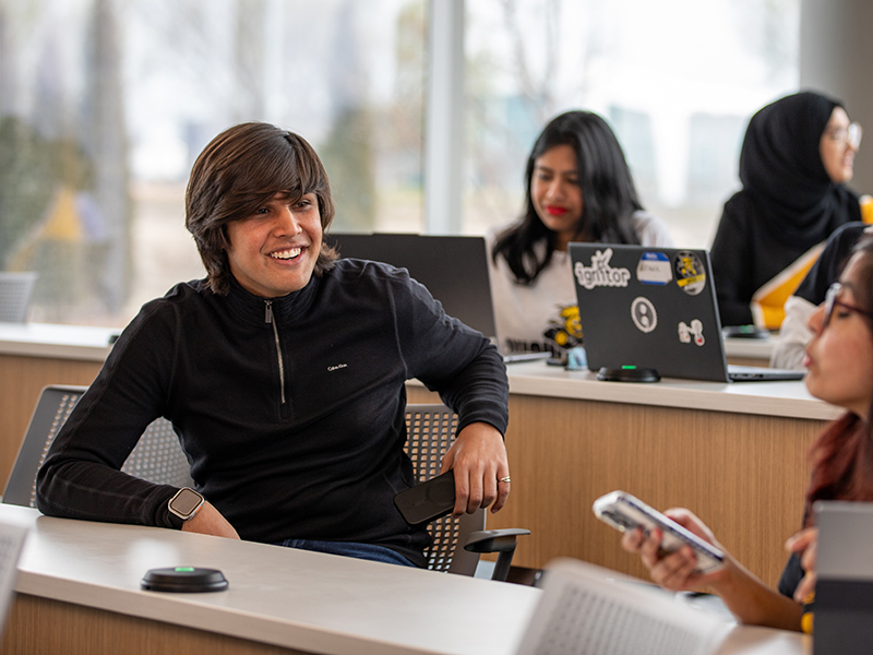 A smiling student sits in a classroom in a relaxed pose