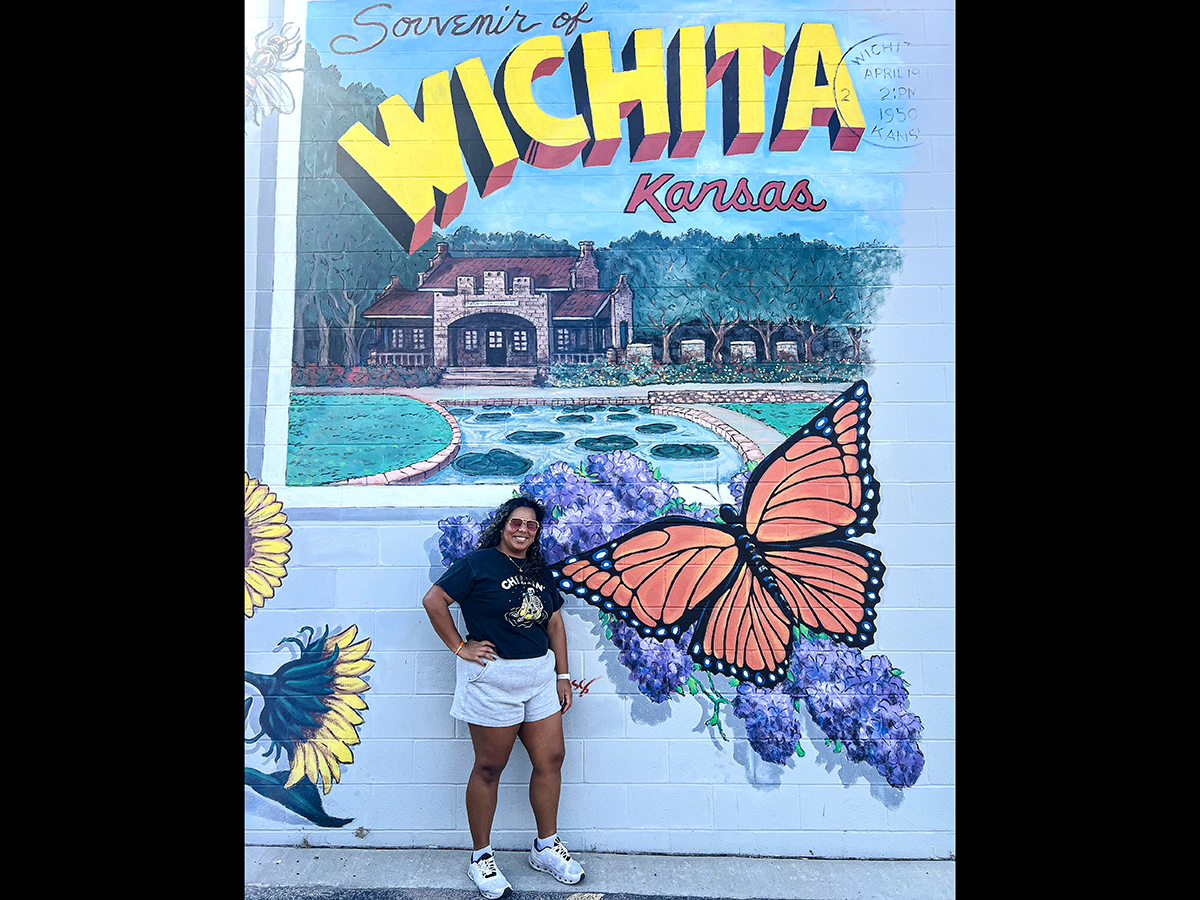 Analiz Rivas posing for a photo next to a "Souvenir of Wichita, Kansas" mural.