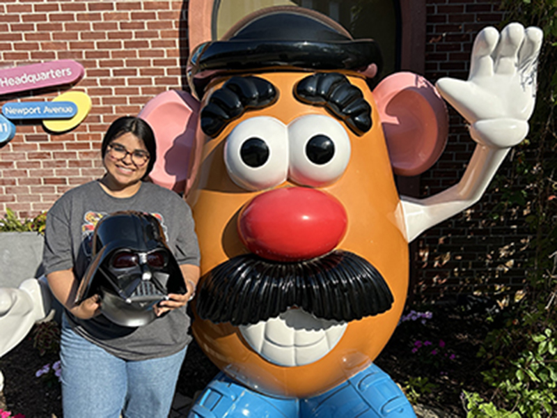 Nataleigh poses beside a giant statue of Mr. Potato Head while holding a Star Wars Darth Vader helmet at her Hasbro internship in Rhode Island.