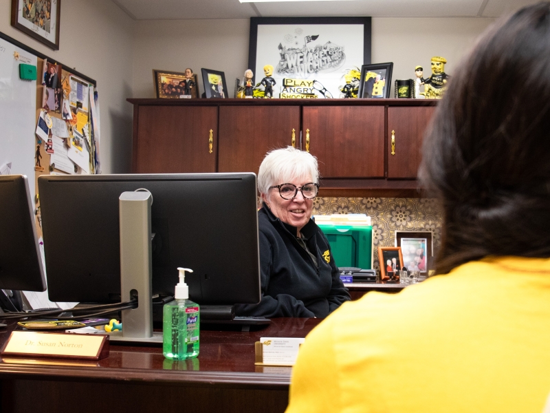Wichita State advisor assists student with Wichita State decor in the background.