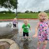 Three children play in rain puddles