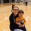 A staff member smiles with a child on a basketball court.