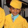 A young boy smiles on graduation day in a yellow cap and gown. 
