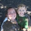 A child and staff member covered in mud smile.