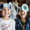 Two children smile while wearing paper hats.