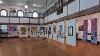 Art work is hung on white panels suspended from the ceiling.