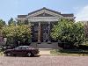 The exterior of The Kansas African American Museum, a columned building with a peaked roof that sits on a street paved with bricks. 
