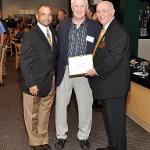 Two men present a third with a plaque