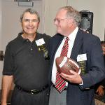 Two men pose, one holds a football