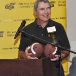 Speaker at a podium holding two footballs