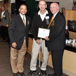 Two men present a third with a plaque