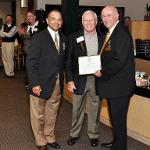 Two men present a third with a plaque