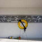 Closer shot of monument, showing the names of lives lost. In the foreground, a wreath commemorating the 50th observance is visible.