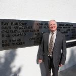 A man stands beside his name on the black plane addition to the monument