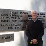 A man stands beside his name on the black plane addition to the monument