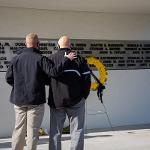 Two men stand in front of the memorial, one has his hand on the other's back