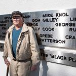 A man stands beside his name on the black plane addition to the monument