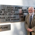 A man stands beside his name on the black plane addition to the monument