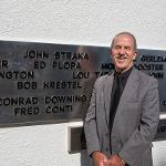 A man stands beside his name on the black plane addition to the monument