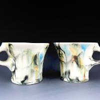 A pair of mugs that have small handles. The mugs have smoky clouds of color on top of primarily white glaze.