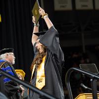 A student holding their diploma about their head while on stage during commencement.