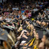 A row of graduates sitting during the commencement ceremony. You can see graduates from a few different colleges by the color of their tassel.