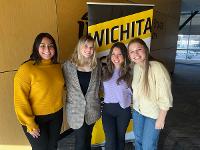 Four gore scholars pose for a photo while standing in front of a Wichita State banner.