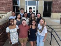 Eleven students gather on the steps of the Marcus Welcome Center for a group photo