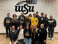 A group photo in front of a patterned backgroup with a WSU logo.