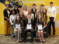 A group of current Gore scholars and Gore alumni pose in front of a yellow mural in the Marcus Welcome Center.