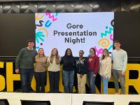 Eight students pose in front of a projector screen that says "Gore Presentation Night!"