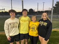 Four students in Shocker gear pose for a photo on a kickball field.