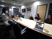 Three Gore Scholars are seated at a conference room table across from two admissions staff members. A laptop, tripod and light kit are set up for the virtual DSI info session they're hosting.