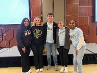 A group of Gore scholars poses for a picture in front of a podium in the Rhatigan Student Center ballroom.