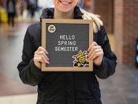 A student stands in the Rhatigan Student Center holding a First Day of School sign.