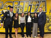Five Gore Scholars pose for a photo in front of a yellow Wichita State mural in the Rhatigan Student Center