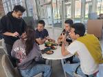 A group of five people sit chatting, eating, and competing, on Venture Valley.