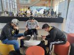 Three competitors sit together playing in front of the table of food.