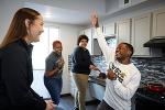 Four students hang out in a kitchen at the Flats at WSU. One student is acting silly and pretending to sing into a whisk while the other students laugh.