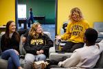 Four students lounge in a The Flats at WSU common area. One student is perched on an arm rest while telling the other students a story.