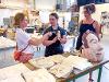 An instructor points at a clay mold being held by Brookelle Peterson. On the table in front of them sits a variety of clay molds as well as a large paper sculpture of a head.